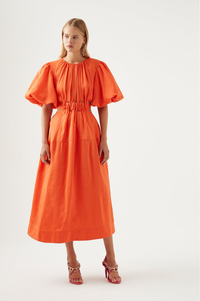Woman wearing Aje Cosette Tie Back Midi Dress in orange with short puff sleeves, crew neckline and drawcord detail at waist with tie up at back.